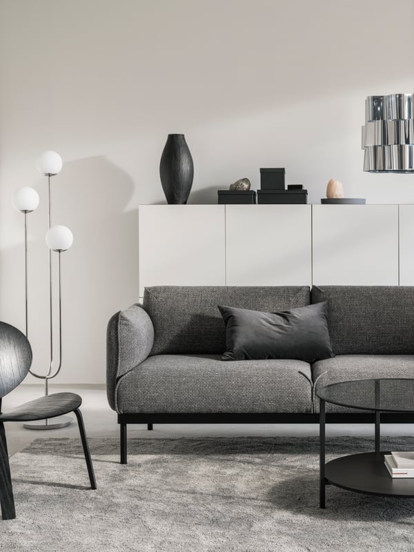 A living room with white walls, a grey/black ÄPPLARYD sofa, an easy chair, a coffee table and white storage units.