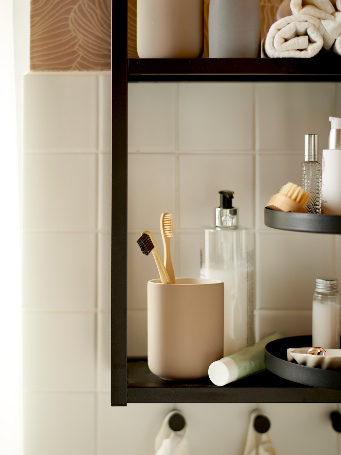 A beige EKOLN toothbrush holder stands on a black ENHET shelf together with other bathroom items and towels.
