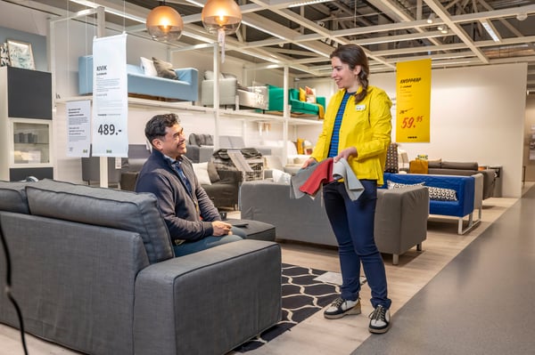 A customer trying a dining chair while a co-worker offers guidance in the furniture showroom.