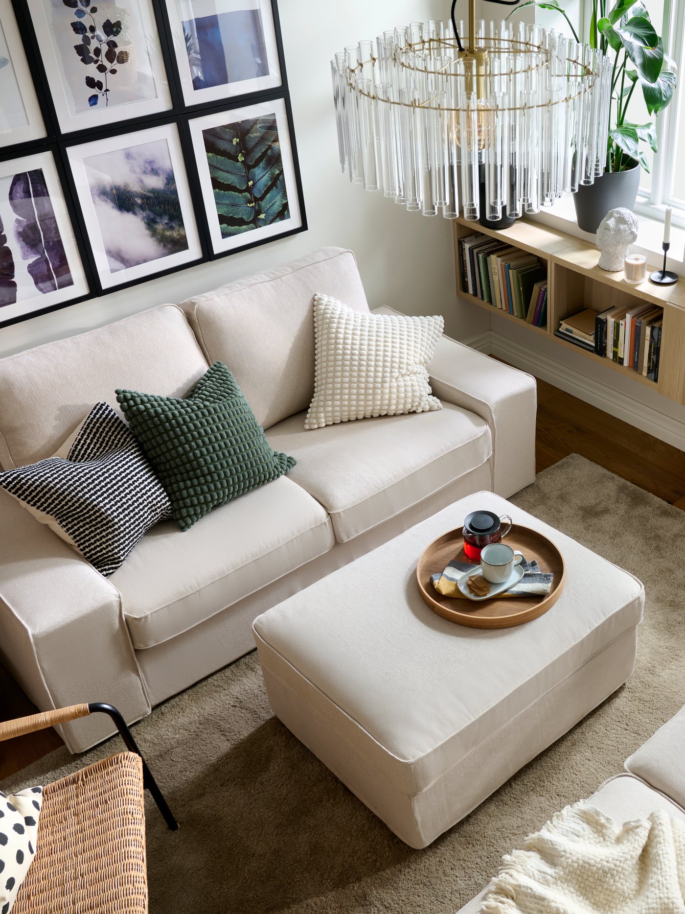 A living room with facing KIVIK two-seat sofas with colourful textiles, a pouffe in-between, and neatly arranged wall art.