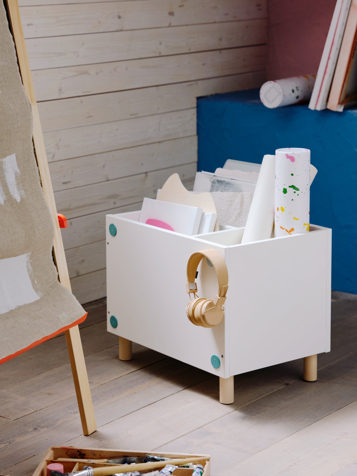 A children's room with a white SMUSSLA bedside table/shelf unit used as storage for drawings and hanging earphones.