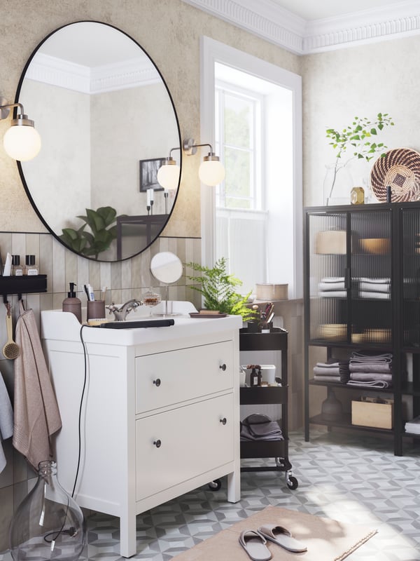 LINDBYN ogledalo visi između dve FRIHULT zidne lampe iznad belog HEMNES/RÄTTVIKEN postolja umivaonika s dve fioke.