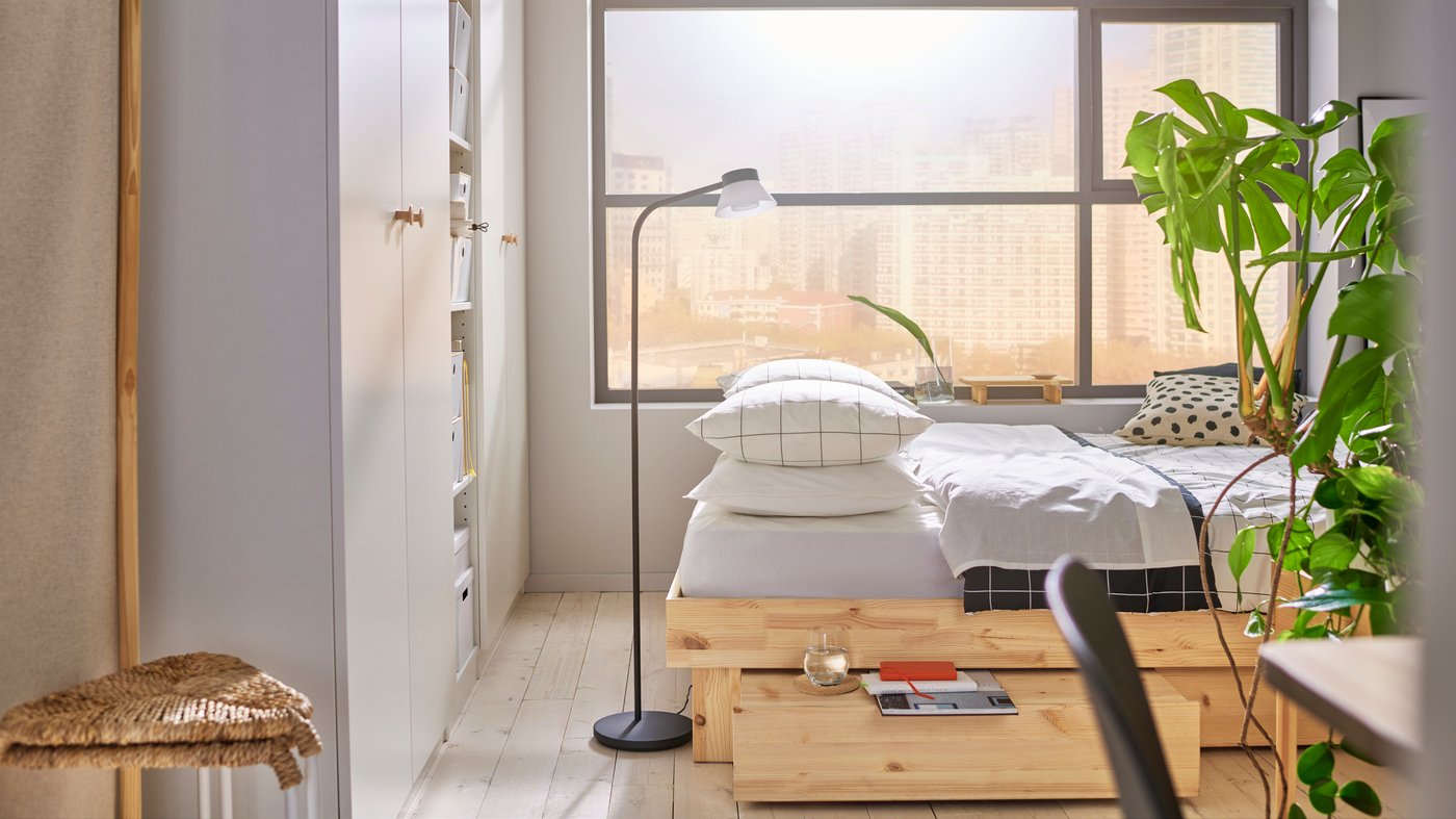 Recámara en colores beige con una cama GLAMBERGET y un gran ventanal detrás de ella. Clósets blancos a la izquierda.