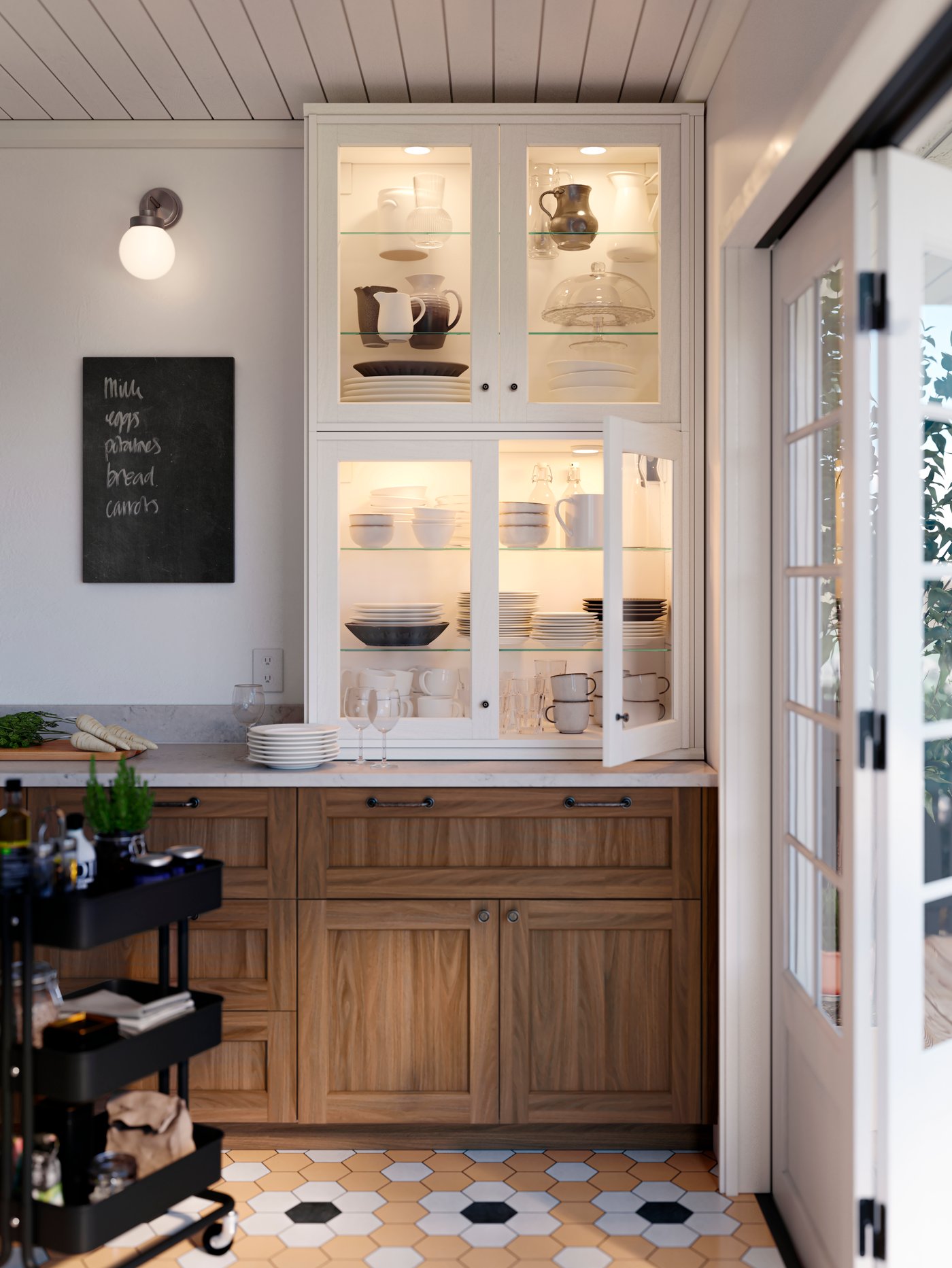 Una cocina con frentes de cocina de nogal ENKÖPING, una encimera de cocina llena de vajilla y utensilios para servir y un carrito negro.