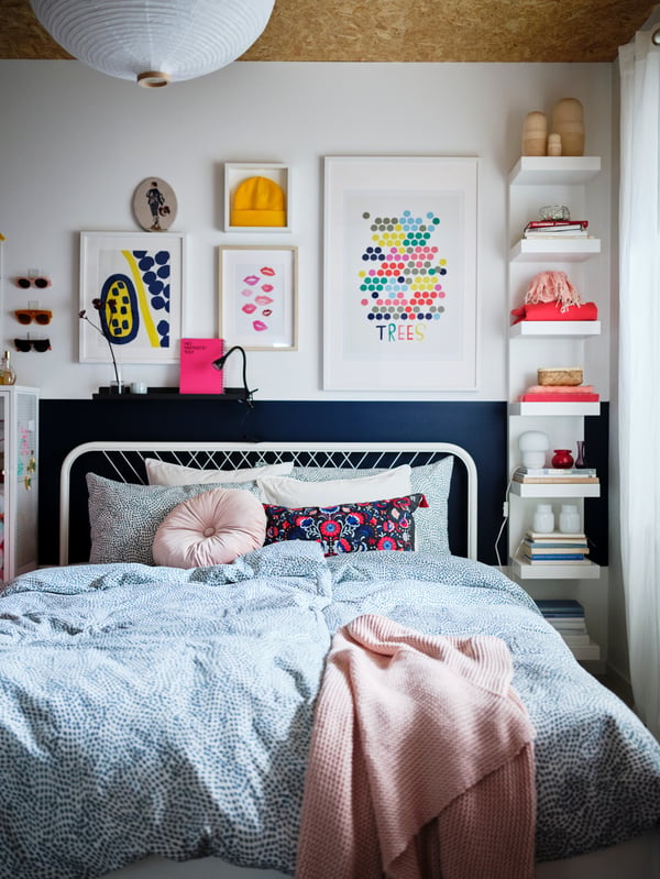 Une chambre aux tons doux et aux décorations colorées, et un lit NESTTUN blanc avec du linge de lit TRÄDKRASSULA bleu/blanc.