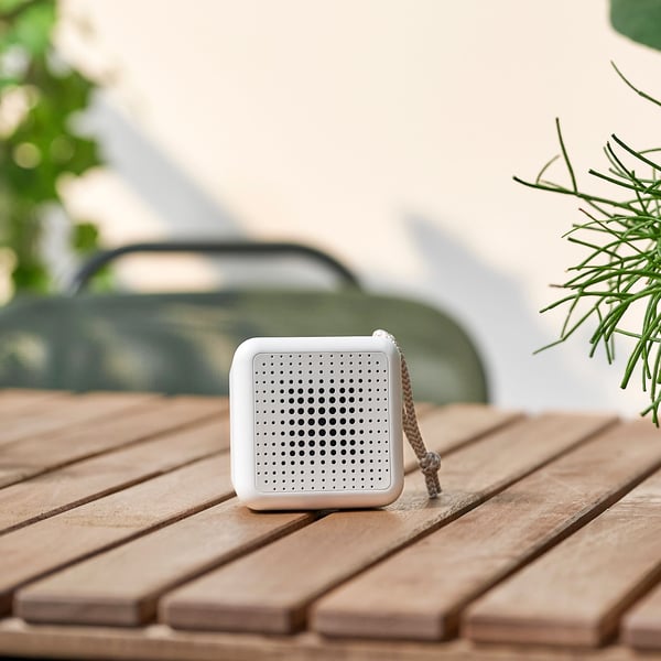 En hvid vandtæt og transportabel VAPPEBY Bluetooth-højtaler står på et bord på en altan på en solrig dag.