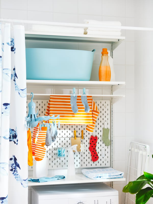 A laundry area with a TORKIS laundry basket, a SKÅDIS pegboard, a hanger with pegs and laundry on a BOAXEL shelf unit.