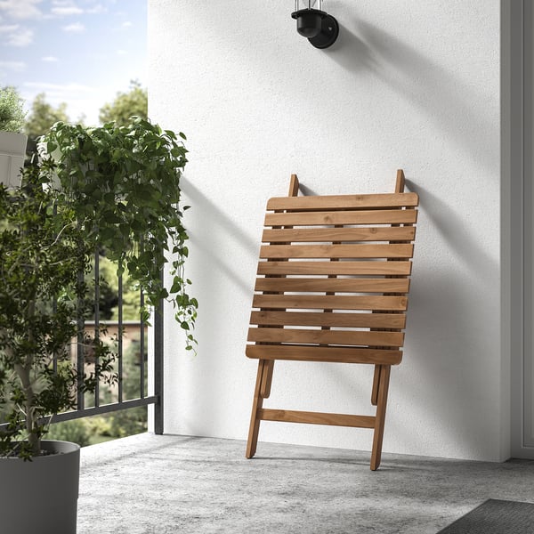 Wooden folding chair against a white wall on a balcony, with a hanging plant beside it.