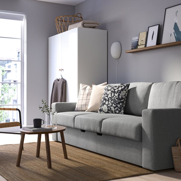 Modern living room with grey sofa-bed, throw pillows, cabinet, coffee table, and shelf with pictures.