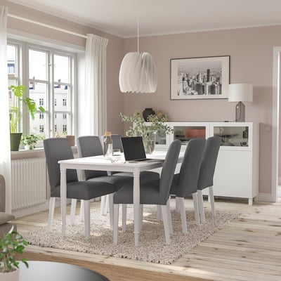Modern dining room with white DANDERYD table, grey chairs, laptop, vase, lamp, and city photo. Windows allow natural light. Cosy yet airy feel.