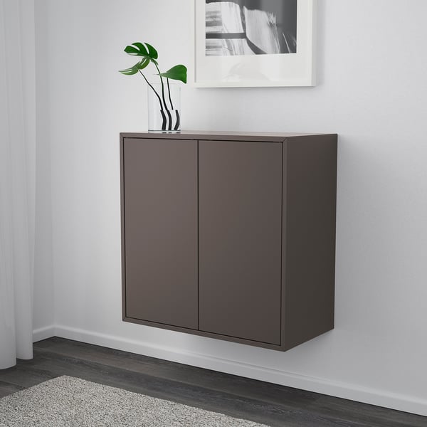 Dark brown wall-mounted cabinet with two doors, holding a white vase with green plant on top, below a framed picture on a white wall.