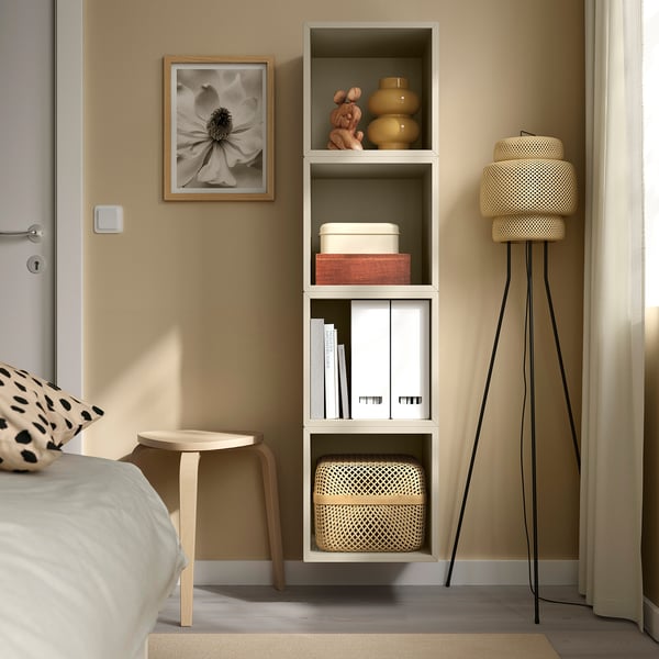 Small, white EKET wall unit stores books, decor; fits neatly beside bed.