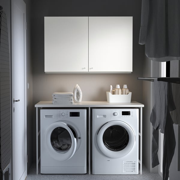 Modern laundry setup with ENHET cabinet, washing machine, dryer, towels, iron, and clothes rack.
