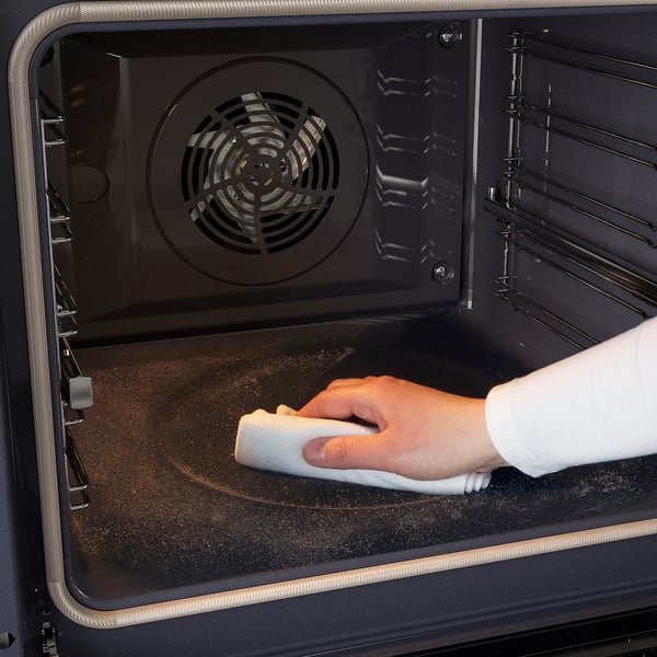 Cleaning oven interior using self-cleaning function. Hand holding cloth, wiping base.
