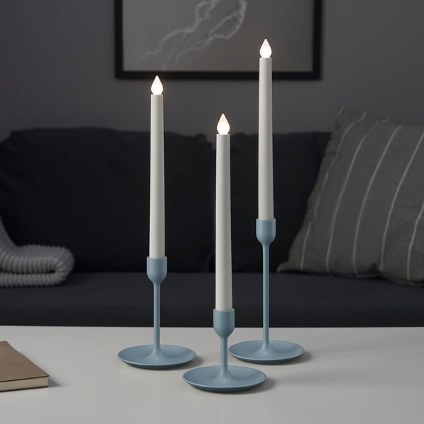Three lighted candles of varying heights on blue holders, adding cosy ambiance to a living room.