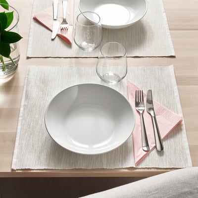 Two table settings with white plates, silverware, glasses, and pink napkins on beige placemats.