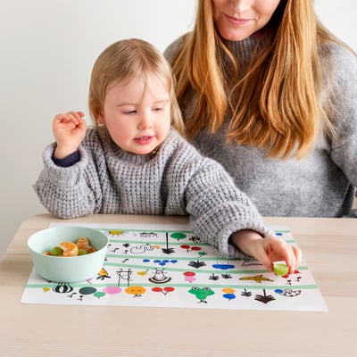 Child and adult with GRÖNFINK place mat. Mat teaches colours, shapes, protects table.