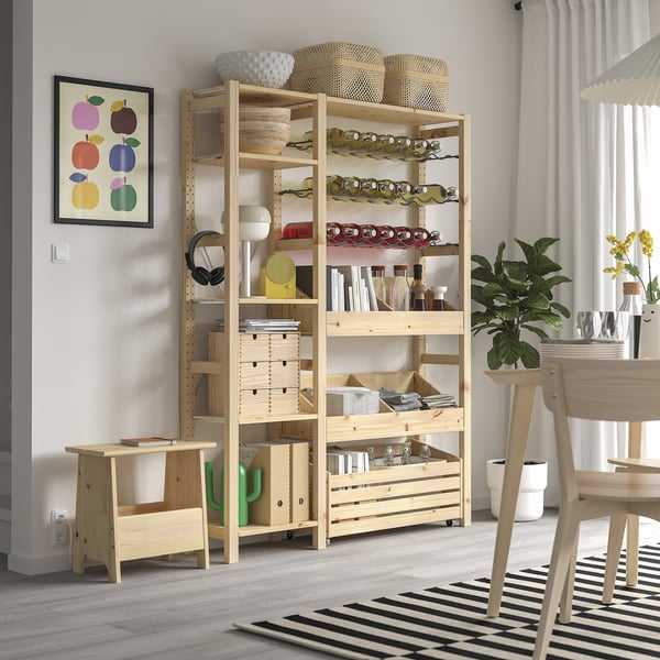 Wooden IVAR storage unit with pine shelves, holding vases, books, and wine in a modern room with a striped rug.