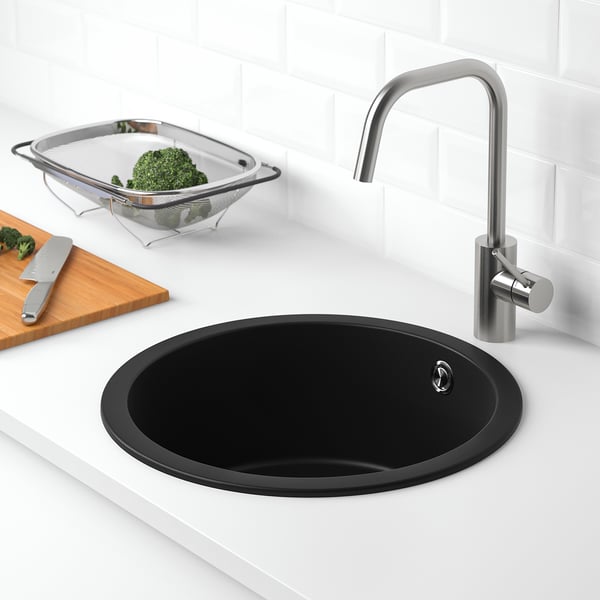 Black sink with quartz countertop, chrome tap, knife, colander with broccoli.
