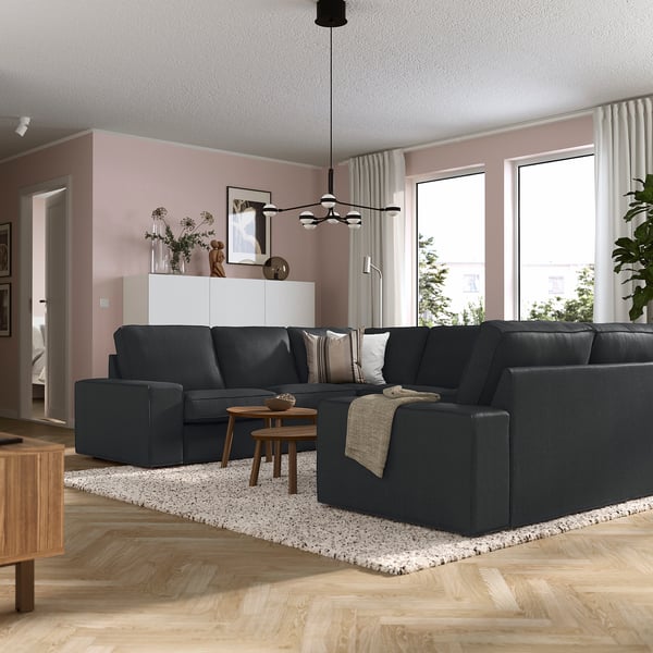 Modern living room with large grey KIVIK sofa, wooden coffee table, and pink walls. Sofa is big, fitting multiple people comfortably.