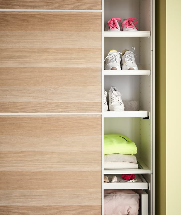 Wooden closet with white shelves, pink trainers, folded clothes, neon-green shirt.