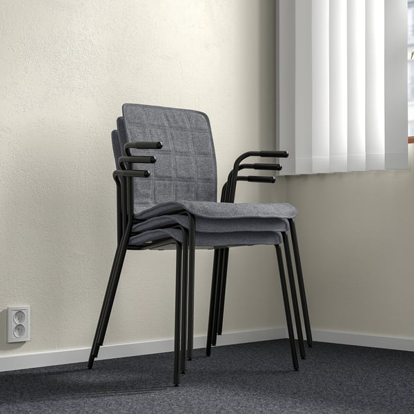 Stacked grey fabric chairs with black metal frames against a wall. Lighting shows gentle shadows, indicating three-dimensional positioning.
