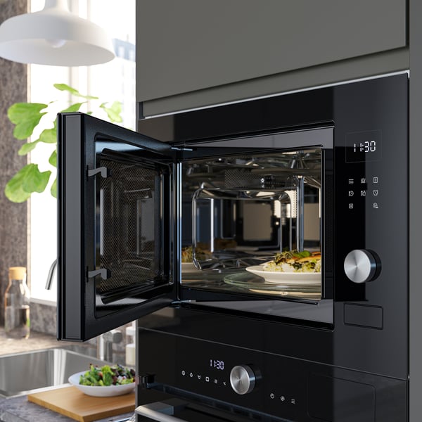 Black built-in microwave with digital display open, showing an oven mitt holding a dish inside.