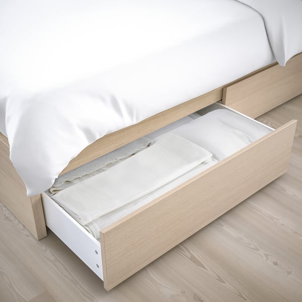 Bed with open drawer, showing storage space. Light wood, white linens.