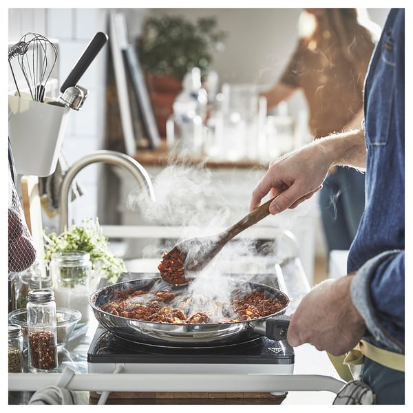 A chef stirs sizzling food in a blue pan on a stove in a kitchen.