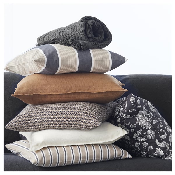 Pile of grey-beige cushions, yarn-dyed, square-shaped with zip, displayed on sofa.