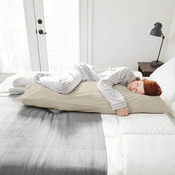 Person sleeps on large,rectangular NONNEA pillow, light beige, crisp white bedding.