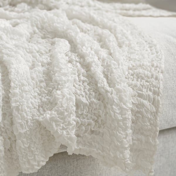 White textured throw blanket draped over furniture, showcasing soft, stretchy fabric and intricate knit pattern.
