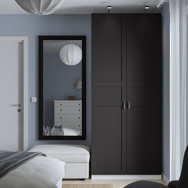 Modern black double-door wardrobe beside mirror, against blue wall.