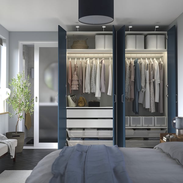 Bedroom closet PAX wardrobe open displaying clothes, shelves, and drawers, with a bed in foreground.
