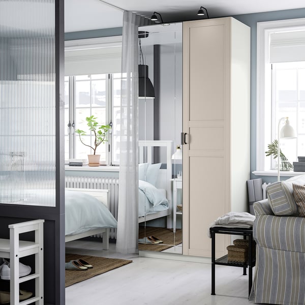 Modern bedroom with PAX wardrobe, mirrored doors reflecting a cosy, windowed space, and a striped sofa.