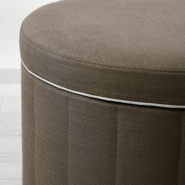 Close-up of a well-crafted, round ottoman with tufted design and grey piping, showcasing high-quality upholstery and stitching.