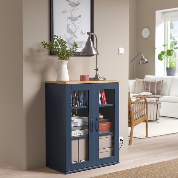 Blue SKRUVBY cabinet with glass doors, rustic handles, and plant nearby.
