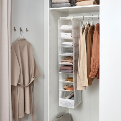 Closet with hanging jacket, folded clothes on white shelves, and hanging garments.