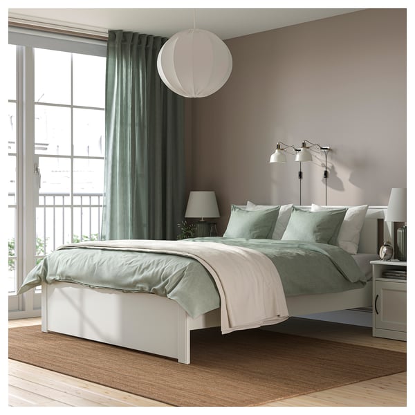Bedroom: white SONGESAND bed with green linens. Large bed, high legs, soft edges. Light green curtains, large window.