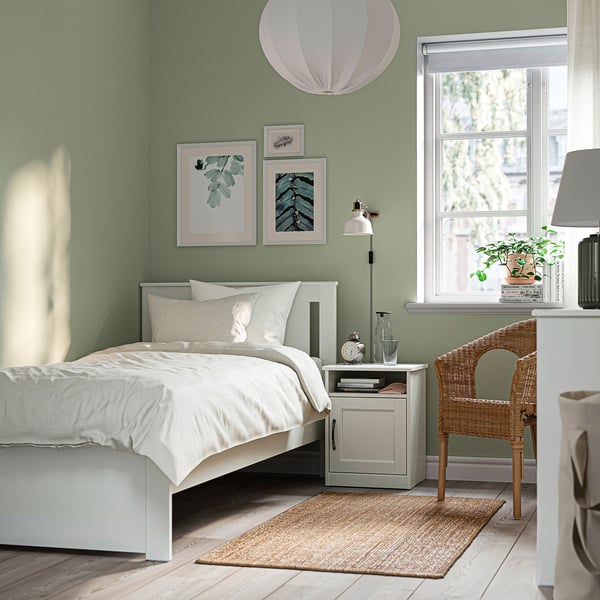 Cosy bedroom with SONGESAND bed, sage walls, crisp linens, rug, bedside table, lamp, plant, wicker chair, art, and large window.