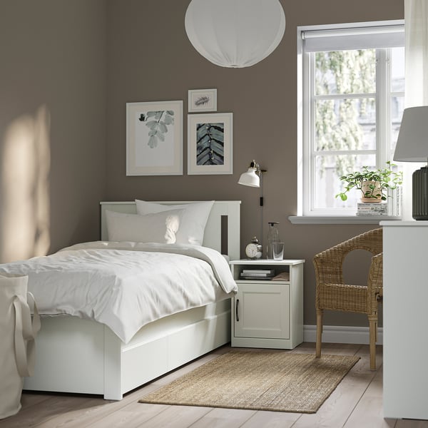 Minimalist grey bedroom with SONGESAND white bed, storage boxes, wicker chair, and large window.