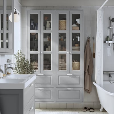 Grey TÄNNFORSEN cabinet with glass doors and drawers in bathroom next to bathtub and sink.