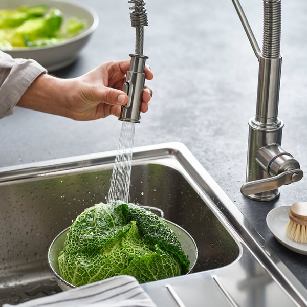 Person washes green vegetables in sink using pull-down kitchen tap with spray function.