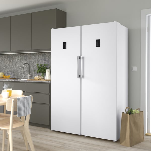 Modern kitchen with TYNNERÅS fridge, dark cabinets, dining table, and chairs. Fridge has led lights and transparent doors. Vegetables nearby.