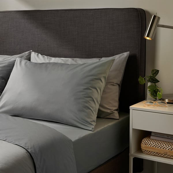 Cosy bedroom with ULLVIDE grey sheets, dark grey headboard, and personal touches on bedside table.