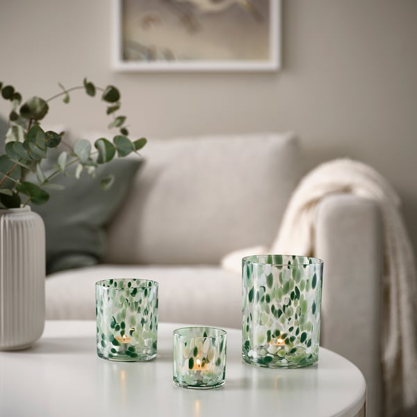 Three VINDSTILLA candle holders vary in size on white table, fourth lit. White couch with pillow and eucalyptus vase in background.