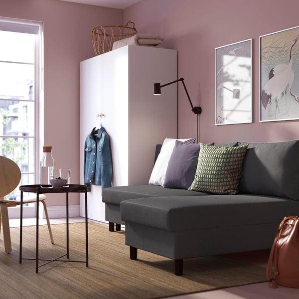 Grå bäddsoffa med kuddar, rosa väggar, guldfåtölj, jeansjacka, sidobordsartiklar.