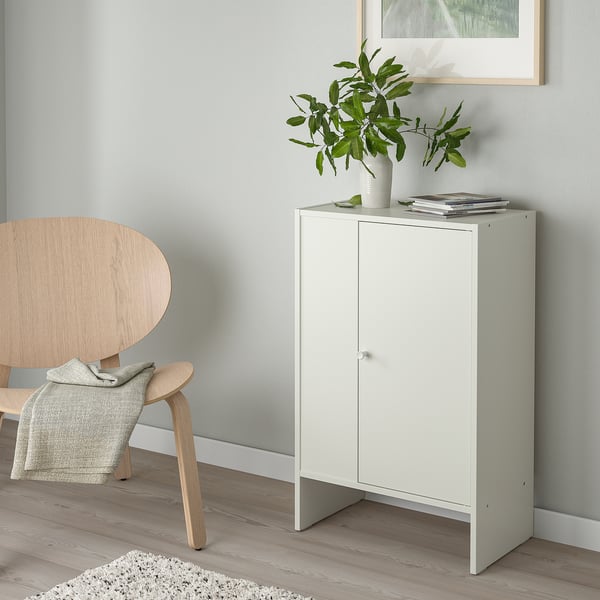 Vitt förvaringsskåp med tidningar och växter. Trästol med filt, minimalistisk inredning.