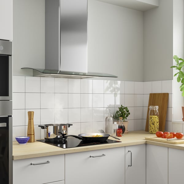 Modernt kök med BALANSERAD fläkt i rostfritt stål, bänkskiva i trä, stekpanna, redskap och krukväxt.