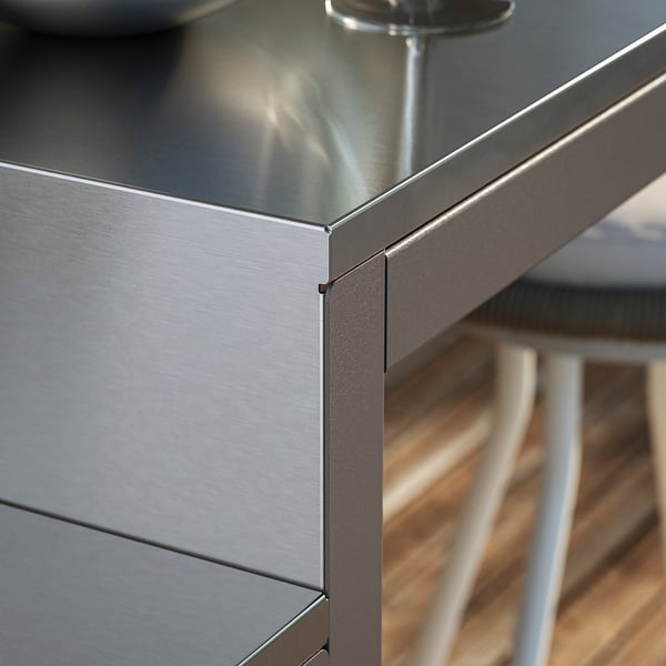 Närbild av modernt utomhusbord med polerad skiva i rostfritt stål och elegant metallram, som visar högkvalitativ finish och hållbar design.